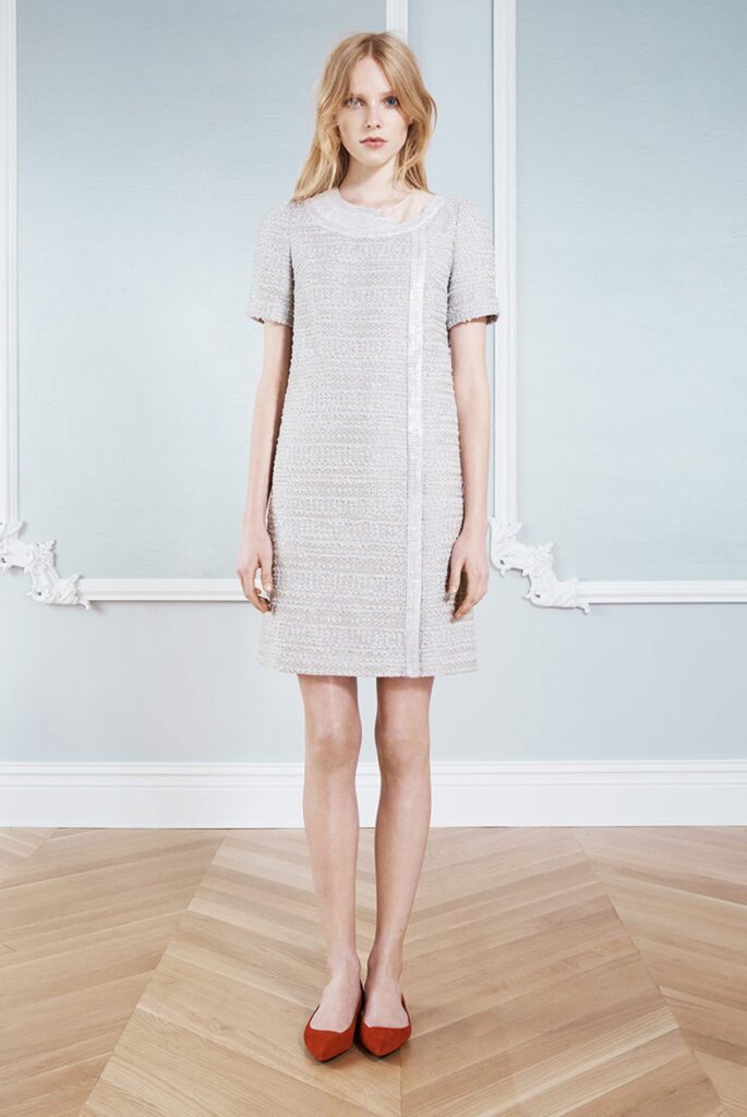 Woman in a short-sleeved, textured light gray dress with red flats, standing on a wooden floor.