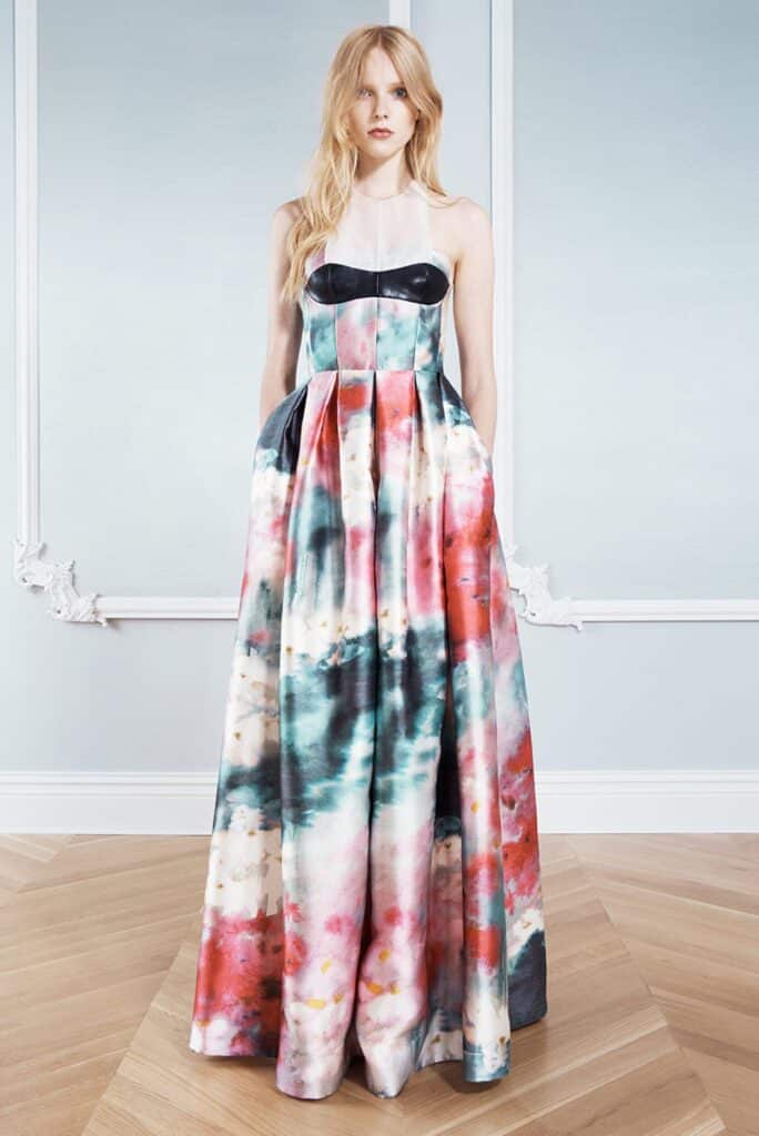 Woman in a sleeveless, floor-length watercolor-print gown with pockets, standing on a parquet floor.