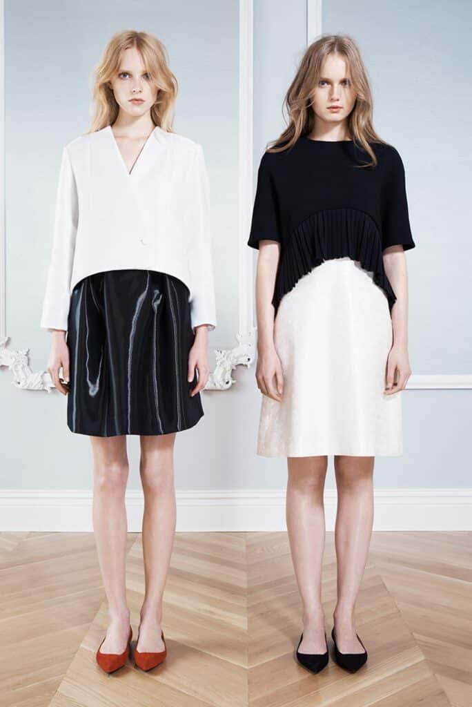 Two women stand side by side wearing black-and-white dresses and flat shoes, posing indoors on a wood floor.
