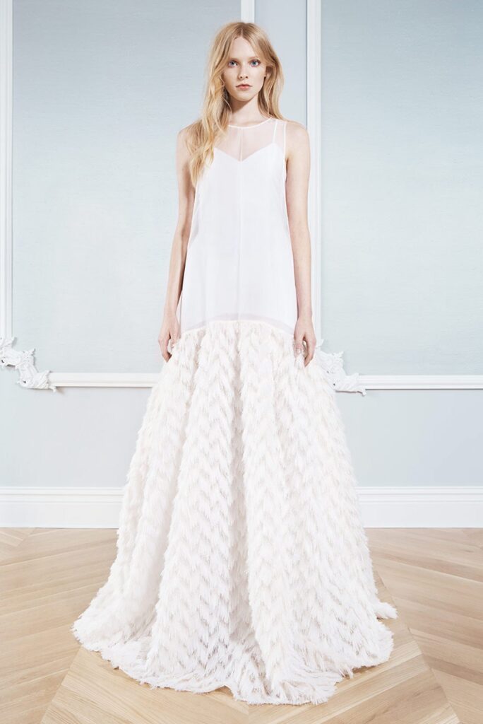 Woman in a sleeveless white dress with a loose top and textured, voluminous skirt, standing indoors.