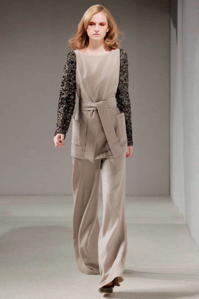 Model wearing wide-leg beige pants, a matching vest with a belt, and a black long-sleeve top.
