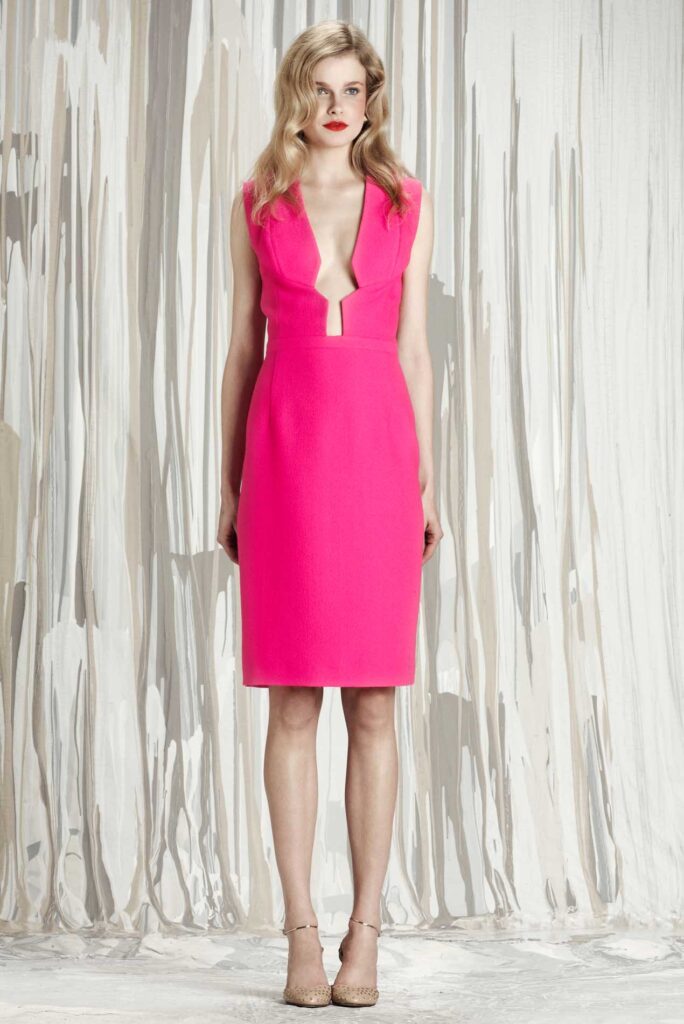 Woman in a sleeveless hot pink dress with deep V-neck standing in front of a white draped background.