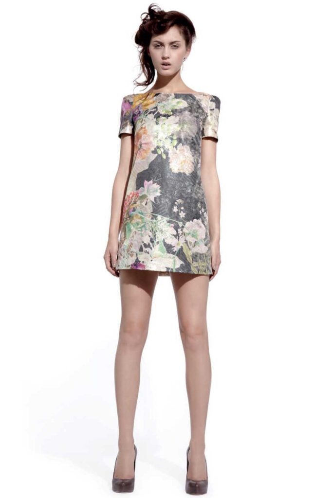 Woman in a short, floral-patterned dress and high heels stands against a plain white background.