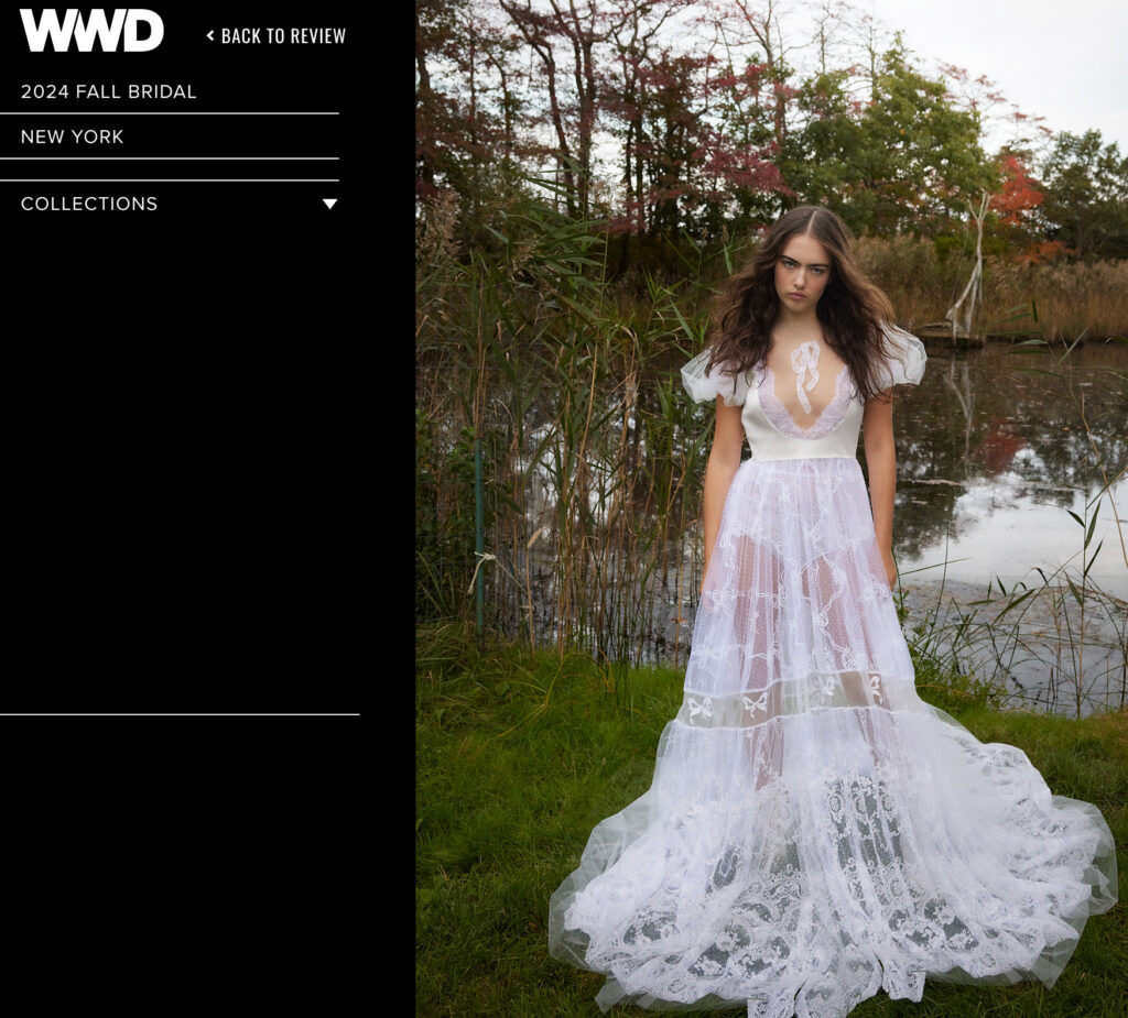 Woman in a white lace bridal gown stands on grass by a pond, surrounded by trees and greenery.
