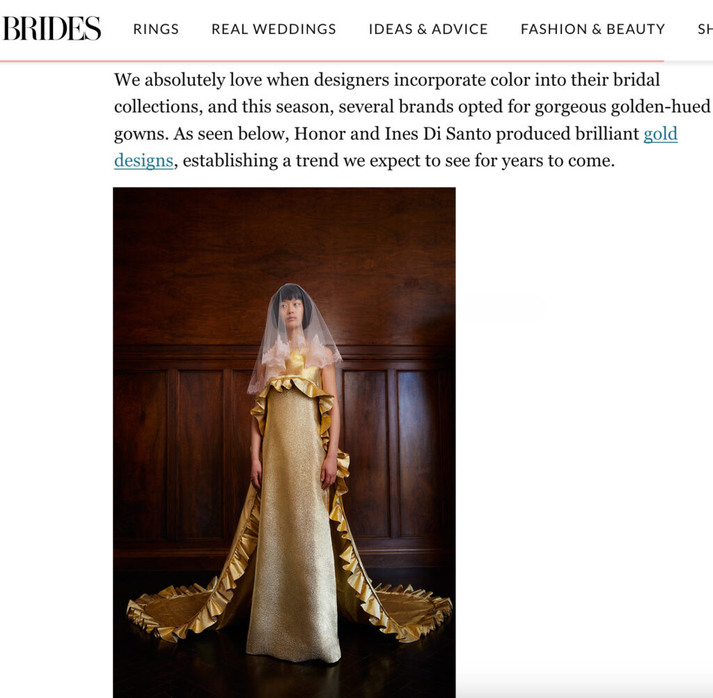 A bride wears a gold ruffled gown with a veil, standing against a rich brown backdrop.
