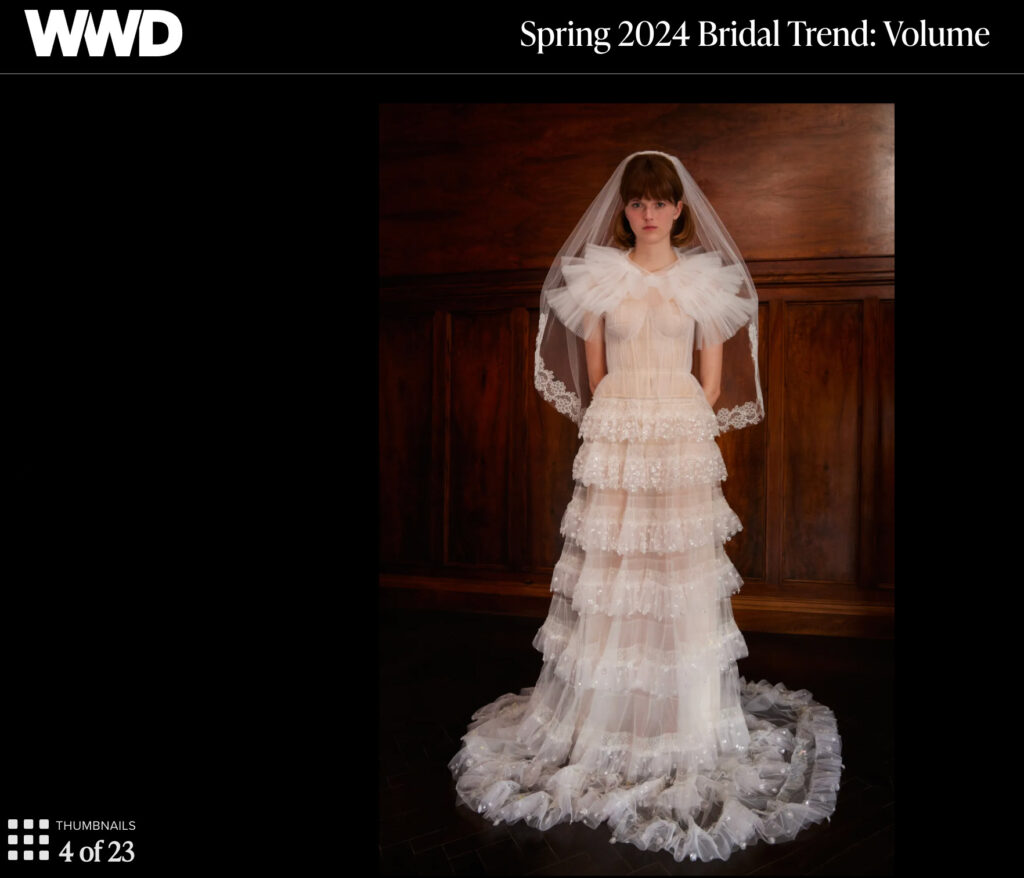 A bride in a tiered, ruffled white gown with a veil stands against dark wood paneling.