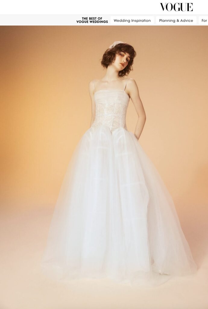Woman in a white, strapless ball gown wedding dress stands against a soft peach gradient background.