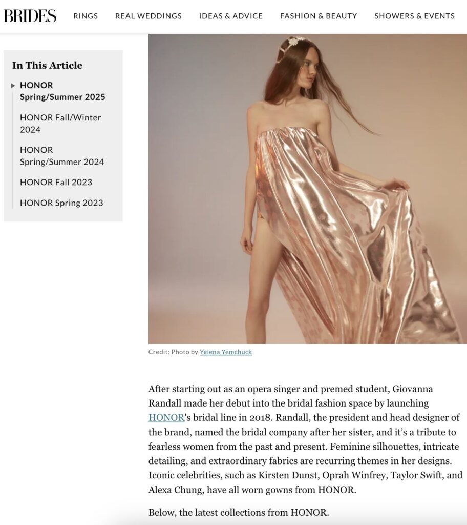 A woman poses in a shiny, strapless gold gown while standing barefoot against a plain, light-colored background.
