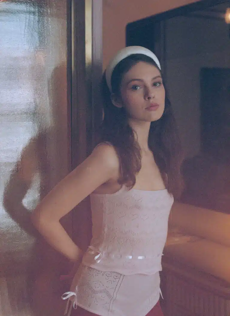 A woman with long brown hair, wearing a Padded Satin Headband and a lace top, stands indoors looking at the camera.