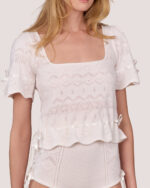 Woman in the Cream Cashmere Heart Knit Top, featuring delicate lace heart patterns and satin ribbon details, square boatneck, slight scalloped trim, and styled with matching knit bottoms.