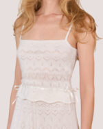 A woman wearing the Cashmere Heart Knit Camisole in Cream, which features heart patterns and satin ribbon details at the waist, facing forward.