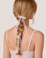 A woman seen from the back with her braid tied using two Dot Lace Bow Hairpins in White. She has paired the pins with the Cashmere Heart Knit Camisole in Cream.