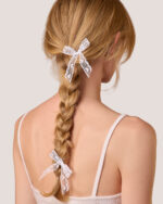 A woman seen from the back, with her braid tied using two white Heart Lace Bow Hairpins and wearing the Cashmere Heart Knit Camisole in Cream.
