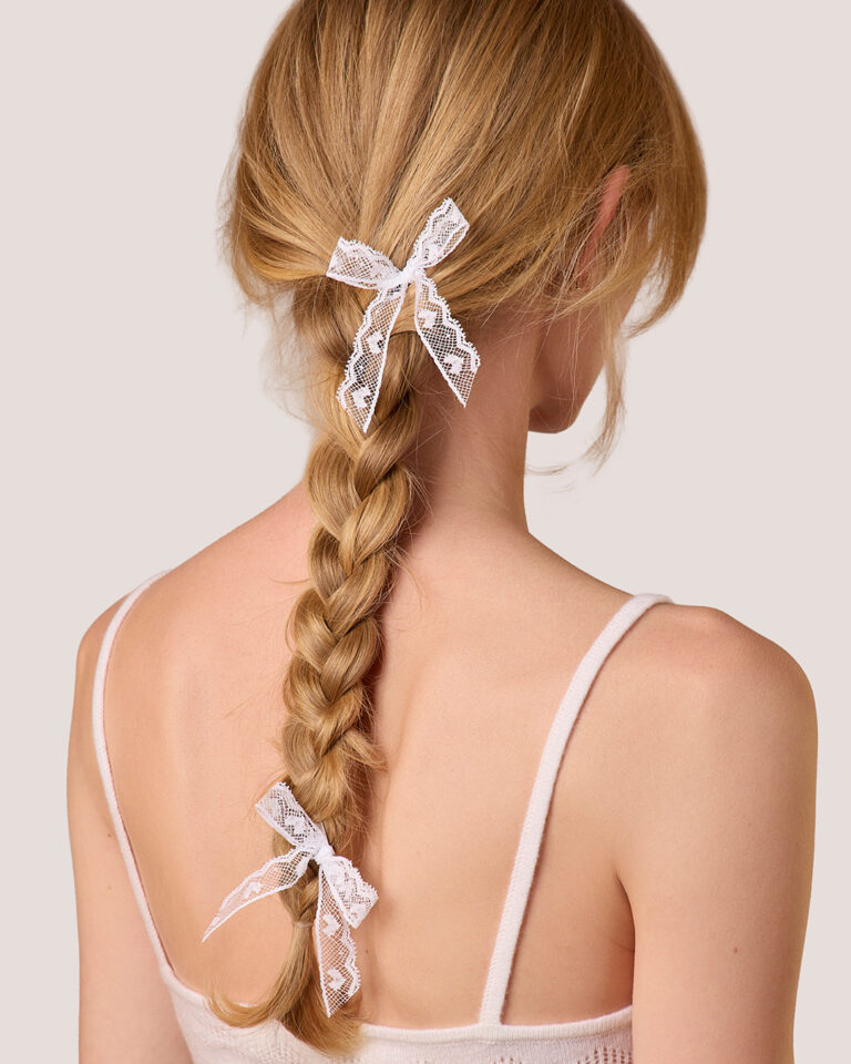 A woman seen from the back, with her braid tied using two Heart Lace Bow Hairpins and wearing a spaghetti strap top.