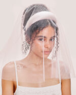 A woman wearing the Embroidered Heart Veil with the Pink Padded Satin Headband and the Cashmere Heart Knit Camisole in Cream, gazes slightly to the side.