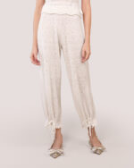 Woman wearing Cashmere Heart Knit Pants in Cream with satin ribbon drawstring hems tied in bows and silver pointed-toe heels with detailing at the toe.
