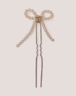 The Pearl Bow Hairpin features a metal pin adorned with a bow crafted from pearl beads and accented at the center with a square gold-colored HONOR "H" logo plate detail.