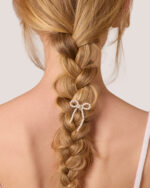 A back view of a blonde braid adorned with the Pearl Bow Hairpin, set against a light background.