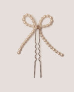 The Pearl Bow Bun Pin is a decorative hairpin featuring a pearl bow design on a metal base pin and a gold-colored HONOR "H" logo on the inside.
