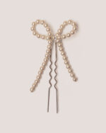A Pearl Bow Bun Pin, crafted from metal and adorned with pearl beads, is displayed against a light background.