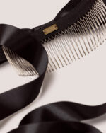 A close-up of the Satin Bow Hair Comb featuring a black satin ribbon, silver metal comb teeth, and a small gold "HONOR" logo nameplate.
