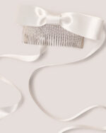 The Satin Bow Hair Comb features a white satin bow on a metal comb with flowing ribbon, shown against a light background.
