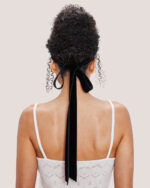 Woman with curly hair in an updo, styled with the Velvet Bow Hair Comb in Black, wearing the Cashmere Heart Knit Camisole in Cream.