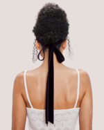 Woman with curly hair in an updo, styled with the Velvet Bow Hair Comb, wearing a white camisole.