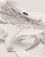 The Velvet Bow Hair Comb in White, featuring a long velvet ribbons, a metal comb attachment, and a gold-colored "HONOR" logo plate, is displayed against a light background.