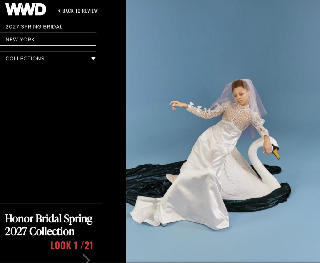 A model in a white bridal gown with a satin skirt and a floral lace bodice with long sleeves and bow detailing poses with a swan prop against a blue background, as featured in a Womenswear Daily (WWD) article.