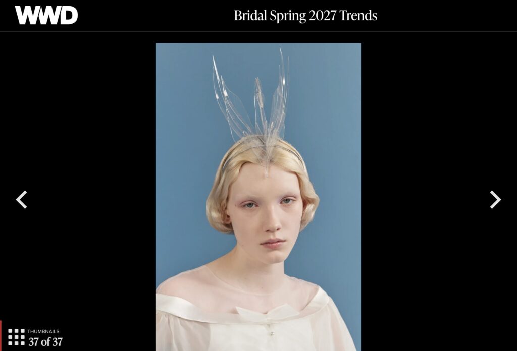 Woman in an off-shoulder white dress and clear swan headpiece poses against a blue background, as featured in a Womenswear Daily (WWD) "Bridal Spring 2027 Trends" article.