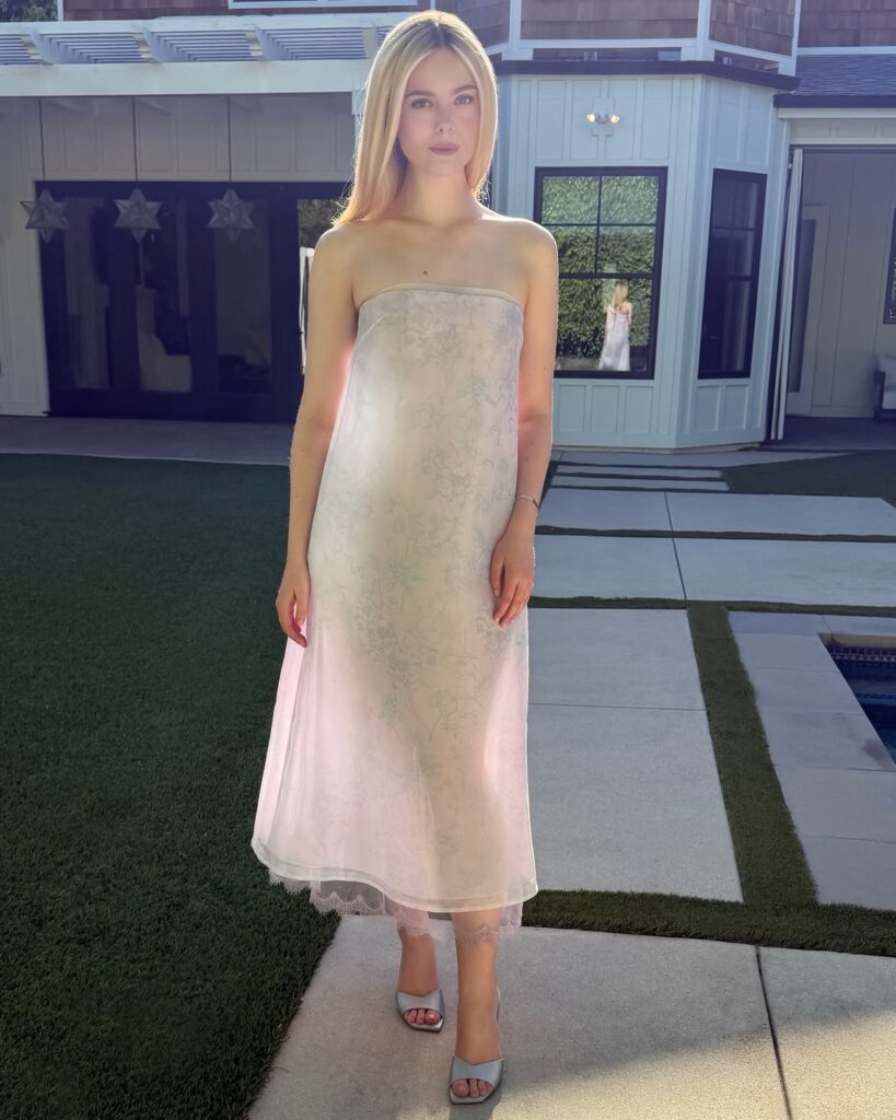 A woman in a strapless, sheer dress stands outside on a patio, with sunlight shining on her.